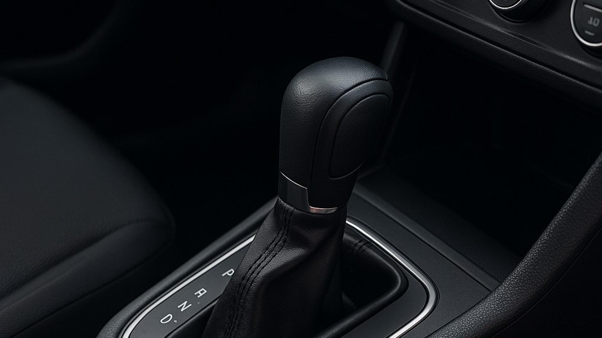 nnenansicht eines Fahrzeugs mit einem modernen Automatikgetriebe. Der Fokus liegt auf dem Schaltknauf des Automatikgetriebes, umgeben von stilvollem, schwarzem Leder und einer klaren Anordnung der Bedienelemente im Fahrzeug.